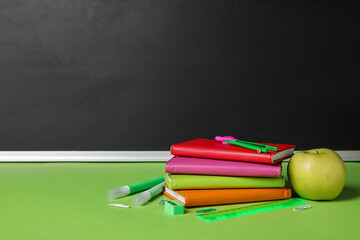 Different stationery and apple on green table against blackboard. Pi Day celebration