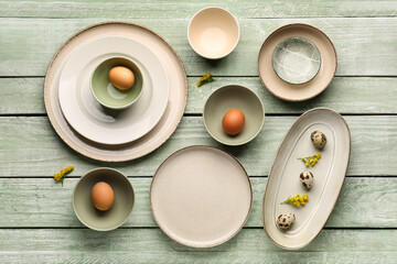 Set of plates and bowls with Easter eggs and floral decor on green wooden background