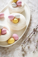 Easter meringue nests with colorful sweet eggs on plate.