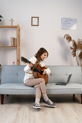 Young woman listening to her online music lessons. Artistic girl playing the acoustic guitar and...