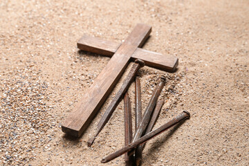 Wooden cross with nails on sand, closeup. Good Friday concept