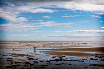 Active couple walking their pet dog along a vast sand beach. Pacific Ocean coastline near Gisborne, New Zealand