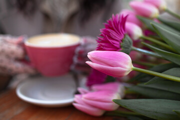  Close---up of female hands in elegant stylish pea gloves hold a mug of a coffee. 35 years old woman is drinking coffee or tea in cafe with a bouquet of flowers in the spring streets of the city. 