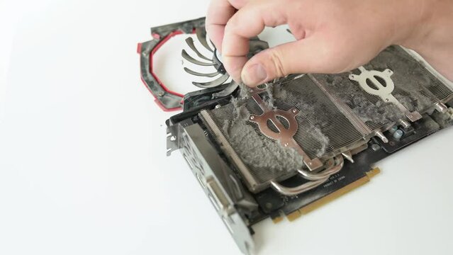 Cleaning the computer video card from caked dust. Close-up computer fans in dirt and dust on a computer graphics card on a white wooden table. A male hand cleans the polluted GPU heatsink for cooler