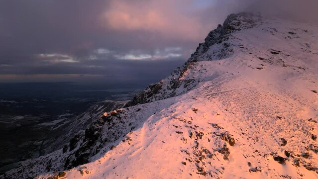 Aerial view of Pen yr Ole Wen mountain with snow under dawn clouds and light