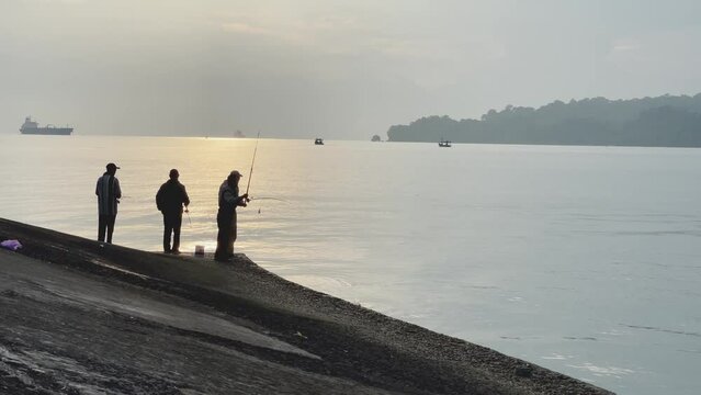 silhouettes of anglers fishing on the pier early in the morning.