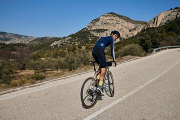 A young male cyclist riding uphill on a gravel bike.Sportsman training hard on bicycle outdoors.Sport motivation.Alicante region in Spain.