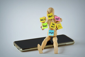 Wooden mannequin with insulting words written on paper notes on smartphone - Concept of cyberbullying