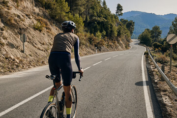 A professional cyclist riding a bike on the empty road overlooking on mountains in Spain.