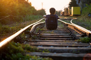 A boy sits on train tracks at dusk