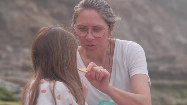 Mature woman with daughter eating cookies on a beach