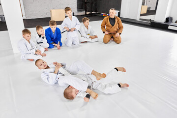 Boys, children in kimonos sitting in circle, watching training judo, jiu-jitsu activity. Learning...