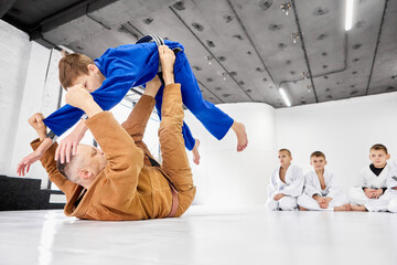 Teacher, professional judo, jiu jitsu coach training kinds, boys, showing exercises. Children learning indoors. Concept of martial arts, combat sport, sport education, childhood, hobby