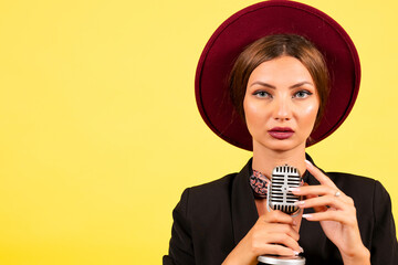 girl in a black suit on a yellow background sings in a retro microphone, portrait, music
