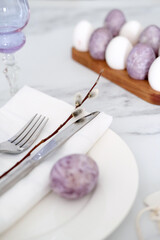 Fototapeta na wymiar Close-up of Easter table setting with purple decorations, willow branches and eggs