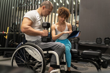 Fototapeta na wymiar A physically challenged person without obstacles workout at the gym with his female fitness instructor.They're making a workout plan.