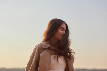 Portrait of a beautiful young woman at sunset. Natural beauty, long hair, woman in a raincoat