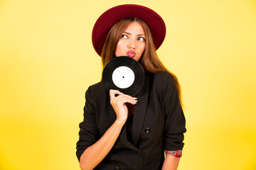 Obraz premium girl in a black suit on a yellow background with a record in her hands, music, the girl shows emotions