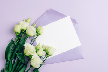 Eustoma grandiflorum white flowers and envelope with blank card on purple background, mockup. Festive background, flat lay, copy space