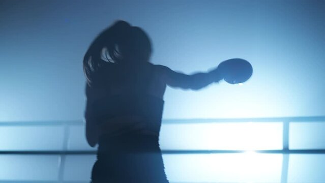 Close-up shot of active woman in boxing gloves warming up before a sparring in the ring. Portrait of determined, female kickboxer training her punch. High quality 4k footage