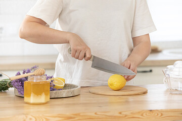 Young woman cutting lemon on wooden board. Preparation of fresh llemonade.
