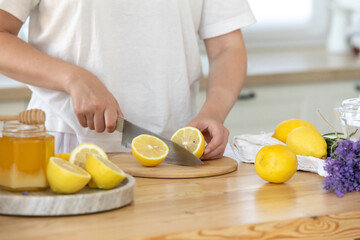 Young woman cutting lemon on wooden board. Preparation of fresh llemonade.