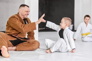 Fotobehang Cooperation. Friendly man, judo, jiu-jitsu coach training with little boys, children. Teaching fight exercises. Concept of martial arts, combat sport, sport education, childhood, hobby © master1305