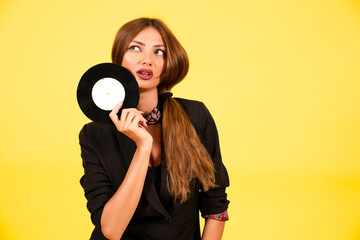 girl in a black suit on a yellow background with a record in her hands, music, the girl shows emotions