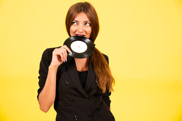 Obraz premium girl in a black suit on a yellow background with a record in her hands, music, the girl shows emotions