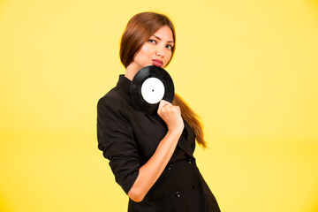Obraz premium girl in a black suit on a yellow background with a record in her hands, music, the girl shows emotions