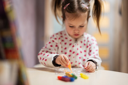 Baby girl with pigtails decorating art with glitter decor tube of paint.