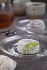 A traditional Japanese fresh homemade rice mochi bun with green tea matcha filling top with matcha powder with pot and cup of tea in background 