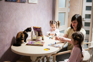 Mother and daughters decorating art with glitter decor. Also cat with them on table.