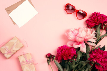 Festive composition with peonies, gifts, a letter and sunglasses on a pastel pink background.