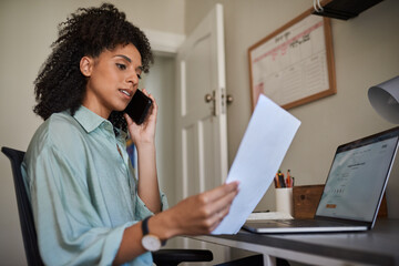 Businesswoman talking on her phone and reading paperwork at home