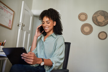 Smiling businesswoman using a tablet and talking on her phone at home