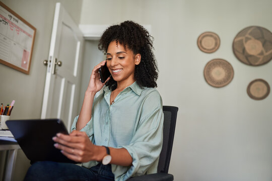 Smiling businesswoman using a tablet and talking on her phone at home