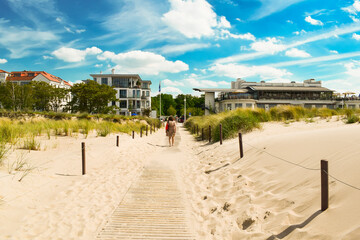 The beach of the Baltic Sea, Germany. Sand, blue sky with clouds, hotels, tall grass. Woman walks...