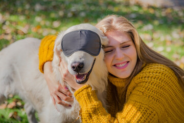 Belgrade, Serbia. November 10th, 2022. Smiling young girl hugging her adorable golden retriever wearing  a black eyes mask in a park on a sunny day.
