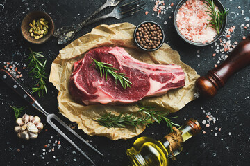 dry aged steak on the bone with spices and rosemary. On a black stone table. Top view.