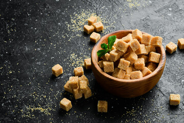 Brown sugar cubes in a bowl. On a black stone background. Rustic style.