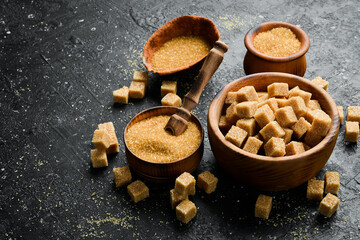 Brown cane sugar in a bowl. Set of sugar. On a black stone background. Rustic style.