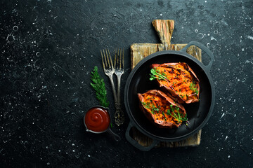 Vegetarian menu. Baked sweet potatoes with spices and garlic in a pan. Healthy food. On a black stone background.