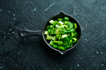 Green onion. Chopped green onion pods in a sauce pan. On a black stone background.