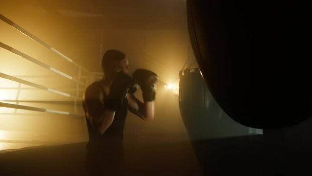 Portrait of a man training his stamina and endurance while punching a bag aggressively. Close-up shot of dedicated sportsman improving his balance and coordination. High quality 4k footage