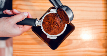 Barista pours coffee bean roaster powder ground coffee pouring into a portafilter with a barista hand at the coffee shop