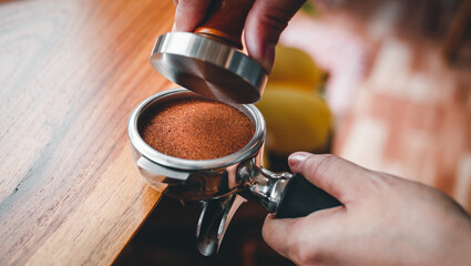 Close-up of hand Barista cafe making coffee with manual presses ground coffee using tamper on the wooden counter bar at the coffee shop