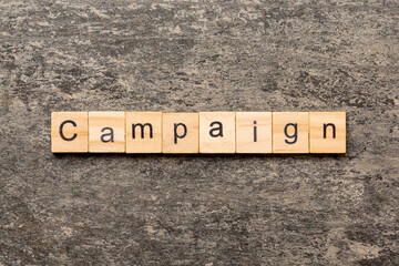 Fototapeta premium CAMPAIGN word written on wood block. CAMPAIGN text on table for your desing, concept