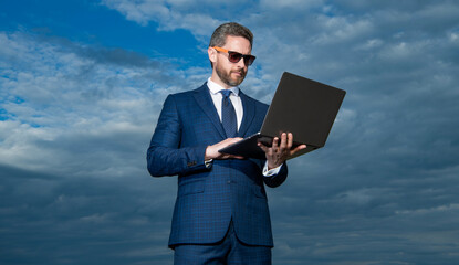 businessman typing on laptop on sky background. businessman with laptop outdoor