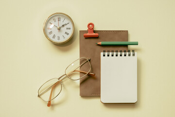 Notepad, diary, clock, eyeglasses, pencil, clip on yellow desk background. flay lay, top view, copy...